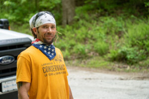 Man in orange shirt and white bandana poses for camera. 